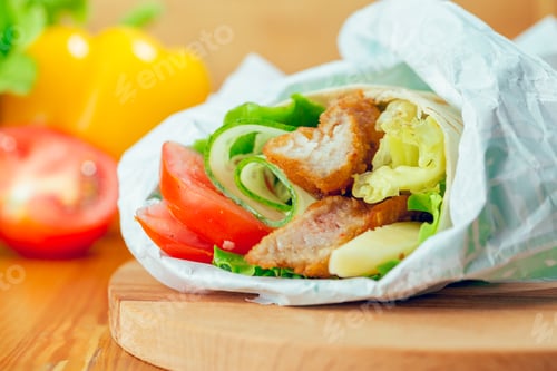 Preview: Fresh wrap filled with grilled chicken, lettuce, tomatoes, and cucumbers on a wooden surface with