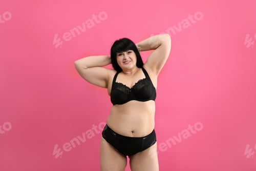 Preview: Beautiful overweight woman in black underwear on pink background. Plus-size model