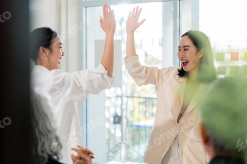 Preview: Businesswomen high-fiving, celebrating successful project completion in modern workplace interior
