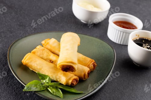 Preview: Overhead view of asian spring rolls on grey plate and condiments on grey background