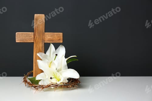 Preview: Wooden cross, crown of thorns and blossom lilies on table against color background, space for text