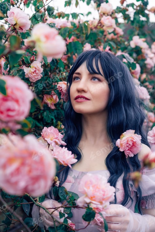 Preview: Fairy tale woman portrait. Young beautiful woman Fairy holds pink flower rose on blooming bush
