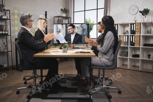 Preview: Group of multiethnical businesspeople clapping hands and looking at screen, having video conference
