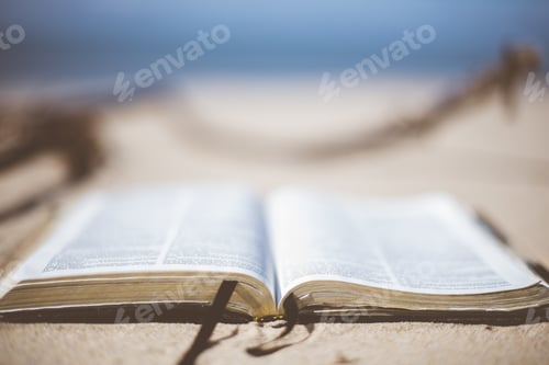 Preview: Closeup shot of an open bible on a sandy surface near the beach with a blurred background