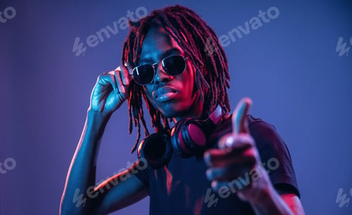 Preview: Pointing by finger, in sunglasses. African American guy is studio with neon lighting
