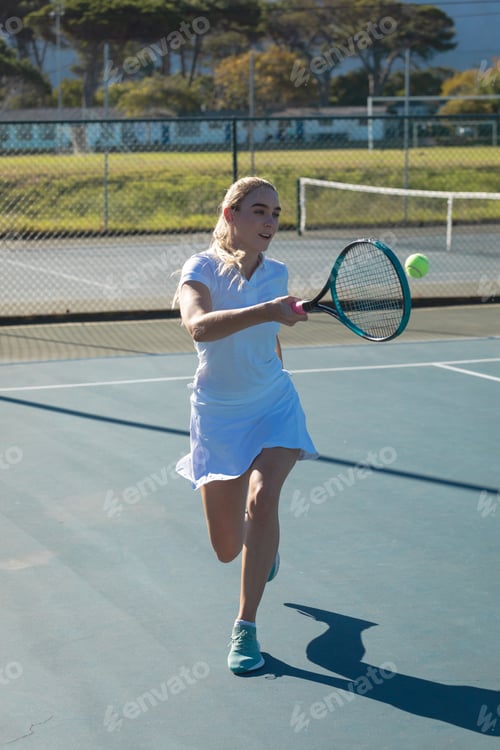 Preview: Full length of young female caucasian tennis player hitting ball with racket at court on sunny day