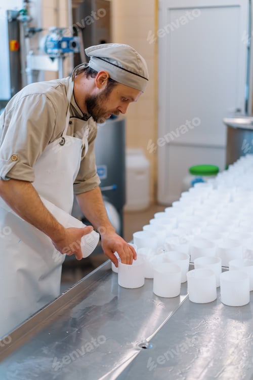 Preview: cheese maker in uniform makes cheese puts molds for pouring cheese production