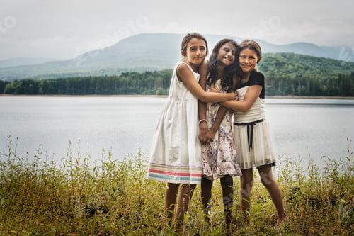 Preview: Three young girls standing by the side of a lake, hugging each other.