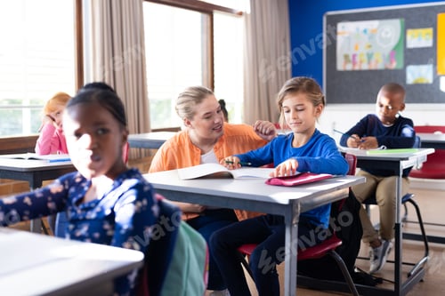 Preview: Helping boy with homework, female teacher in school classroom, other students studying