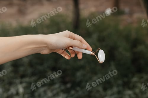 Preview: Hand of Beautician holds cosmetic roller massager for face massage made of rose