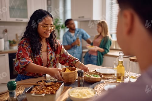 Preview: Happy Indian woman brining food at dining table while making lunch party at home.
