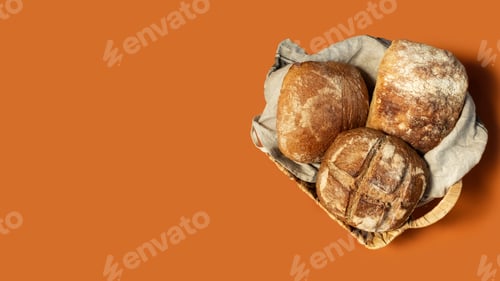Preview: Homemade freshly baked bread lies in a wicker basket on an orange uniform background.