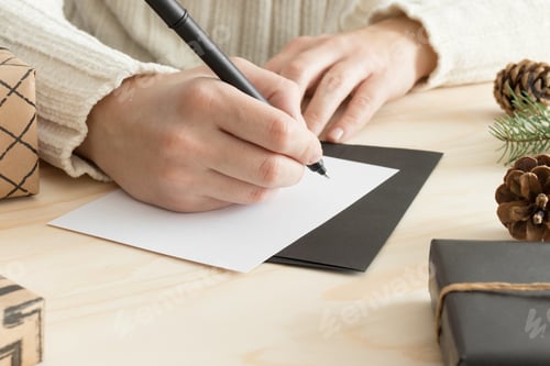 Preview: Woman writing a christmas card on a wooden table with christmas decoration.