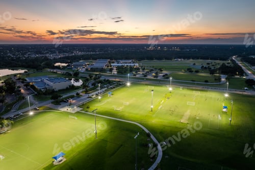 Preview: Sportsmen playing football game on illuminated stadium in public sports park