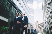 Preview: Smart business partners walking hand in hand to meeting in downtown with smartphone on way