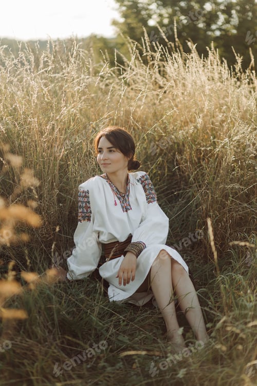 Preview: Young woman in traditional national embroidered shirt and skirt on nature at sunset.