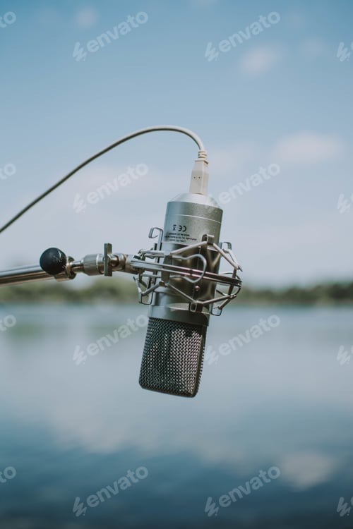 Preview: Vertical shallow shot of gray recording microphone with a wire on a blurred blue background