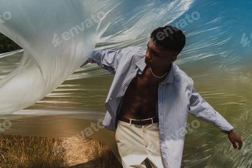 Preview: young african american man in shirt and trousers posing under polyethylene outdoors