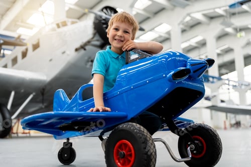 Preview: Portrait of cute little blond happy kid boy enjoy have fun play riding pedal toy plane model against