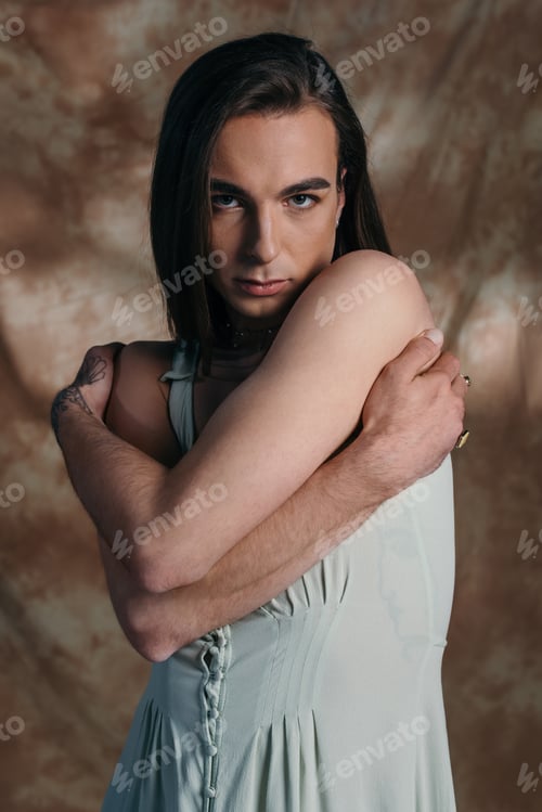 Preview: Portrait of nonbinary person in sundress touching shoulders on abstract brown background