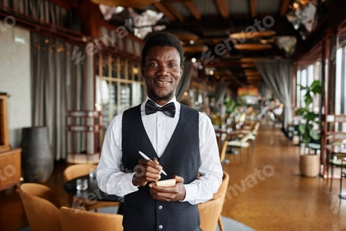 Preview: Young Black man as server in restaurant holding notepad ready to take orders