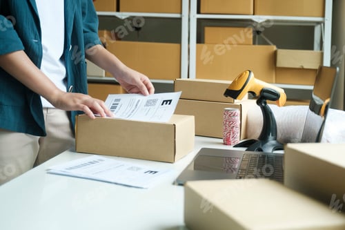 Preview: Young entrepreneur packing online order product for shipping.