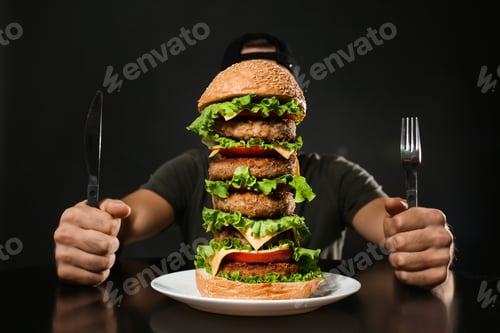 Preview: Man with cutlery eating huge burger on black background