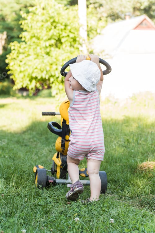 Preview: little girl is carrying her tricycle, holding on to her parent's handle. International Bicycle Day