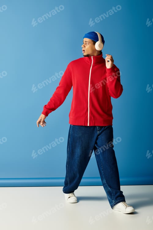 Preview: Stylish young man in beanie and red jacket poses against a vibrant blue backdrop