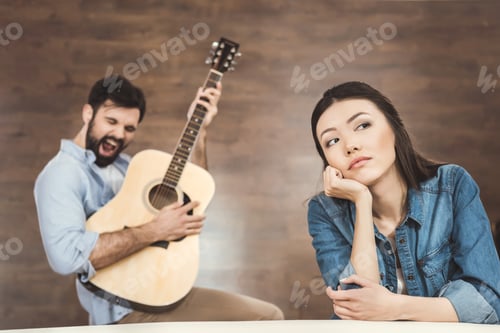 Preview: Woman daydreaming with hand on chin with man playing on guitar on background