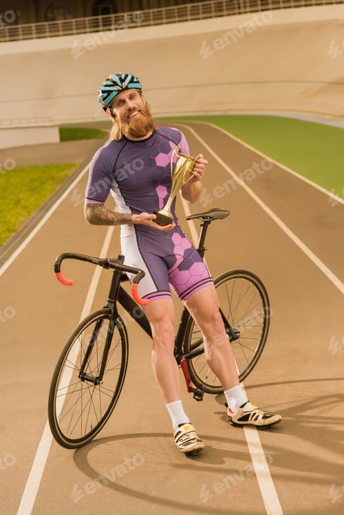 Preview: smiling cyclist with champion cup looking at camera on cycle race track