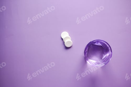 Preview: Effervescent soluble tablet pills and glass of water on purple background