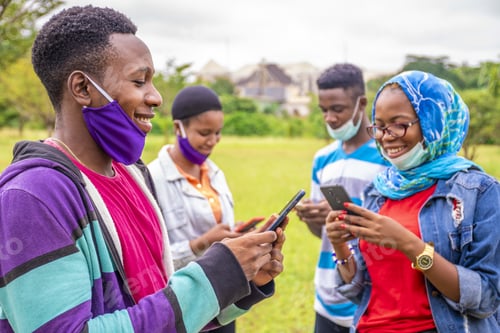 Preview: Group of young African friends with facemasks using their phones at a park