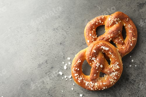 Preview: Tasty pretzels with salt on grey table, flat lay. Space for text