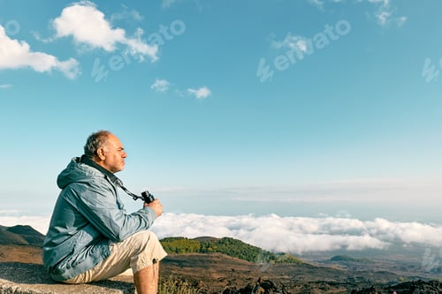 Preview: Mature bearded man looking through binoculars at panoramic view of colorful summits of volcano Etna
