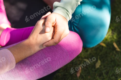 Preview: Midsection of biracial lesbian couple practicing yoga sitting holding hands in garden