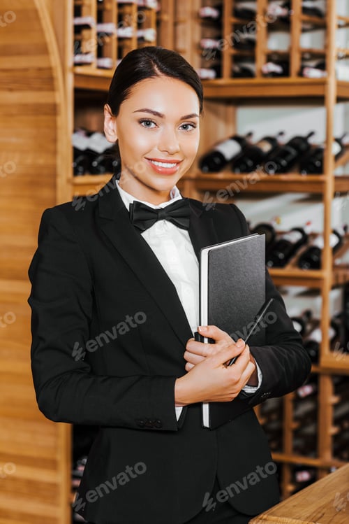 Preview: smiling female wine steward witn notebook looking at camera at wine store