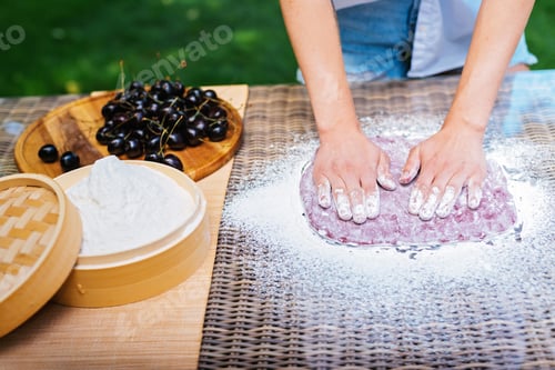 Preview: a person is kneading dough on a table with a bowl of cherries in the background. Mochi asian dessert