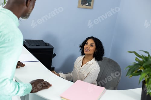 Preview: Biracial medical receptionist sitting at reception desk and talking to african american patient