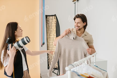 Preview: Photographer and Male Model Picking Fashionable Clothes for Photoshoot in Modern Studio
