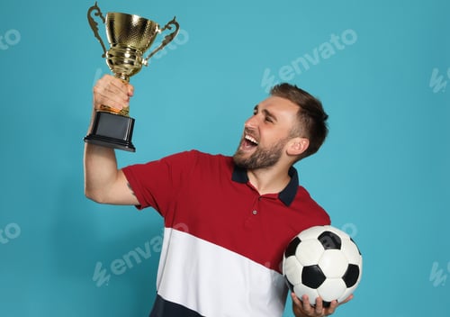 Preview: Portrait of happy young soccer player with gold trophy cup and ball on blue background