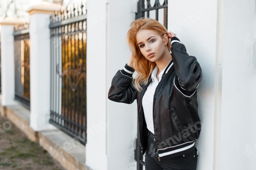 Preview: Pretty beautiful young blond woman in a black spring stylish jacket in white polo. American fashion