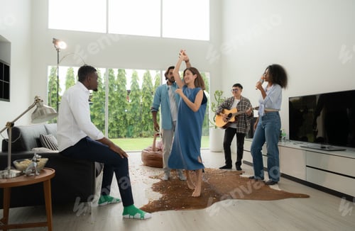 Preview: Group of multiethnic friends having fun at party by playing guitar and singing together at home.