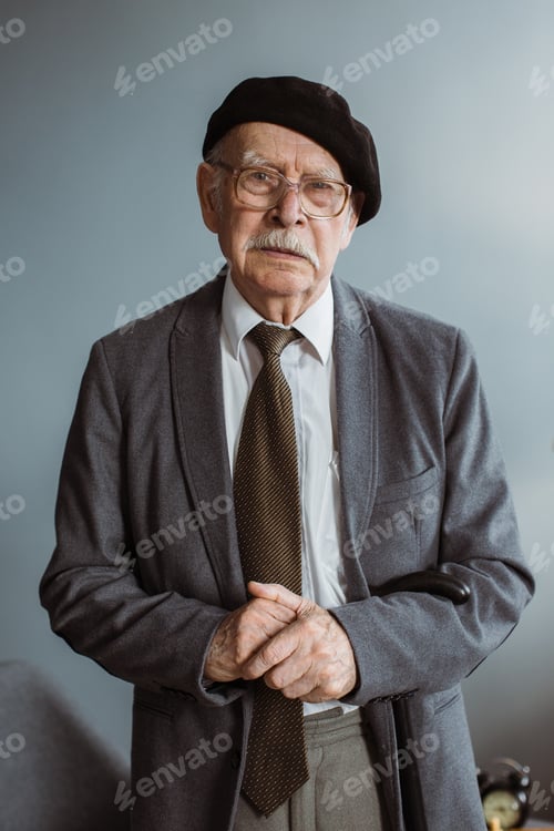 Preview: Portrait of a gray-haired senior man in glasses standing in the living room at home.