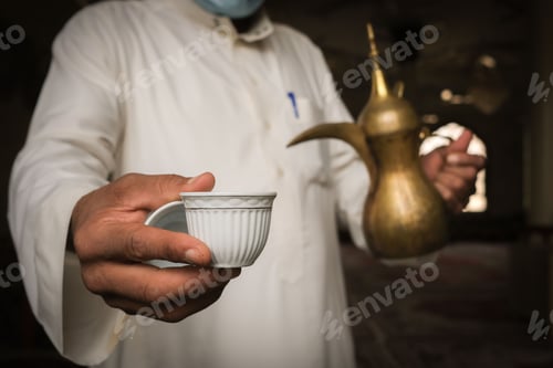 Preview: Middle Eastern man in traditional attire pouring Arabic coffee from a brass dallah into a small cup