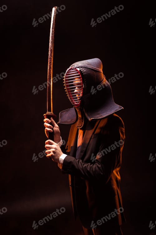 Preview: Kendo fighter in formal wear and helmet holding bamboo sword on dark