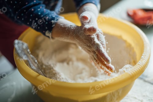 Preview: Hands of a small child stirring flour in a large bowl at home in the kitchen