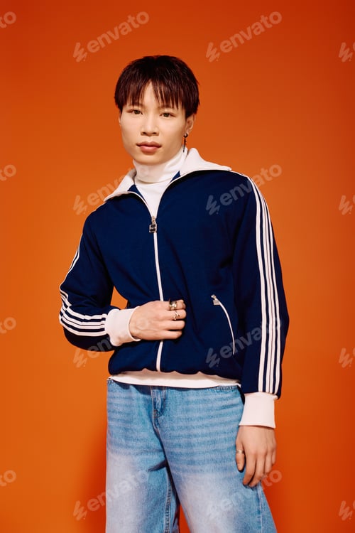 Preview: Stylish asian man posing confidently against a vibrant orange backdrop in urban fashion