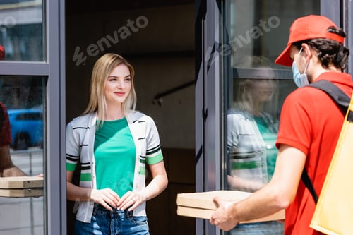 Preview: Selective focus of smiling woman standing near door of building and looking at delivery man in