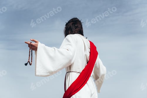 Preview: back view of Jesus in robe, red sash and crown of thorns holding rosary against blue sky